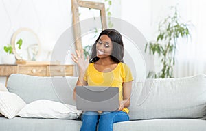 Remote communication concept. Joyful black woman with laptop talking to family, friends or coleagues online from home photo