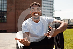 Remote communicaton. Happy black man making video call, gesturing and talking to camera, sitting outdoors in urban area