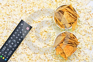 The remote control with buttons lies on popcorn with two paper cups filled with nachos