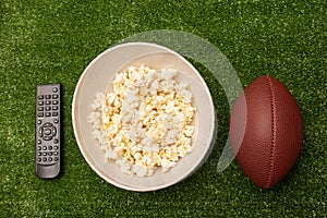 Remote control  pop corn and american football ball on green grass