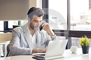 Remote employment or study is a concept. Portrait of a youthful, joyful entrepreneur making a phone call while working on a laptop