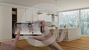 Remote home control system on a digital smart phone tablet. Device with app icons. Interior of minimalist white kitchen in the bac