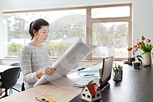 Young woman with blueprint working at home office