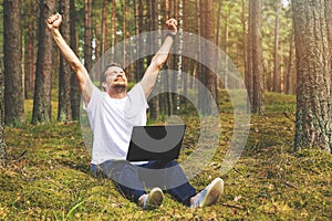 Remote job - man with laptop enjoying working outdoors. hands raised