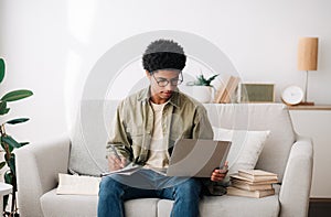 Remote learning concept. Industrious black teen student with laptop computer taking notes during online lecture at home