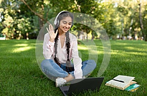 Remote learning. Excited indian female student using laptop, having online lesson and waving to webcam, sitting outdoors