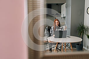 Remote portrait of happy young woman working typing on laptop computer sitting at table smiling looking to screen in