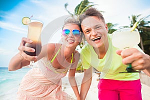 Happy young couple with cocktails having fun by the beach