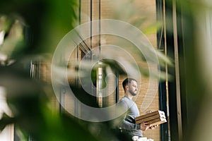 Remote view of delivery man holding boxes pizza and contactless payment POS terminal, standing in entrance hall of