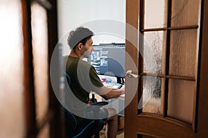 Remote view of focused programmer male working from home office using multiple monitors setup and typing on mechanical