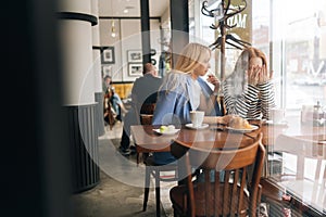Remote view of frustrated young woman and best female friend trying to comfort and cheer up sitting together in cafe