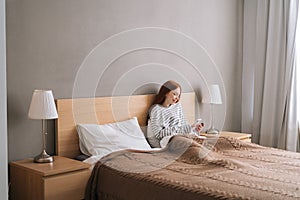 Remote view of happy young woman enjoy shopping online with credit card and mobile phone lying in bed at home.