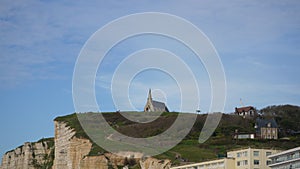 Remote view of small church on Etretat peak at Manneporte and Amont gate, blue cloudy sky on background. Tourists climb