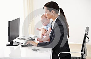 Remote work, businesswoman with her baby and typing on keyboard with pc at her desk in a office. Technology, commitment