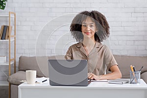 Remote work, study or hobby while self-isolating at home. Friendly african american woman sitting at table with laptop