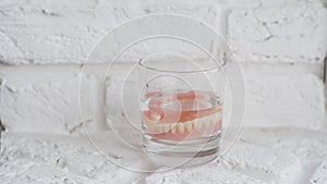 Removable jaw in a glass, close-up. A man`s hand puts false teeth in a glass of solution. Dental care.