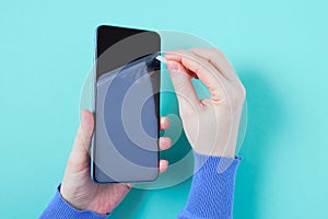 Removes a transparent protective film from new smartphone. Turquoise background