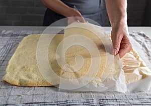Removing baking paper from a fresh baked sponge cake for making swiss roll by a womans hand