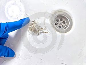 Removing Hair Clog From a Bathroom Sink Drain. Gloved hand extracting hair from a sink