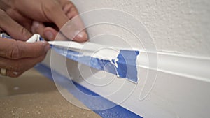 Removing masking tape from molding. A painter pulls of blue painter`s tape from the wall to reveal a clean edge baseboard