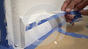 Removing masking tape from moulding. A painter pulls of blue painter`s tape from the wall to reveal a clean edge baseboard