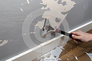Removing silicone paint from a wall damaged by dog claws using a paint and adhesives scraper, womans hand visible.