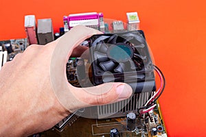 Removing an small old CPU cooler from the motherboard. Human hand dismounting an outdated dusty fan, upgrading processor cooling