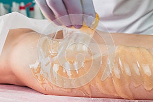 Removing unnecessary hair on the legs. Procedure sugaring in a beauty salon.Depilatory sugar paste