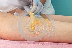 Removing unnecessary hair on the legs. Procedure sugaring in a beauty salon.Depilatory sugar paste