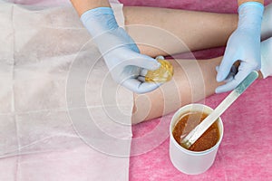 Removing unnecessary hair on the legs. Procedure sugaring in a beauty salon.Depilatory sugar paste