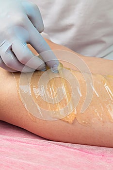 Removing unnecessary hair on the legs. Procedure sugaring in a beauty salon.Depilatory sugar paste