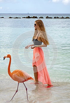 Young Woman with Long Blond Hair in Black Bikini and Pink Wrap Feeding Pink Flamingos on the Beach #3