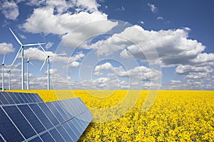 Renewable or green energy concept with wind turbines solar panels and yellow raps field on blue sky with clouds