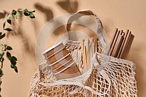 Renewable individual objects for home use, bamboo or paper straws, disposable cups and wooden coffee stirrers on beige with shade