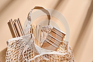 Renewable individual objects for home use, bamboo or paper straws, disposable cups and wooden coffee stirrers on beige with shade