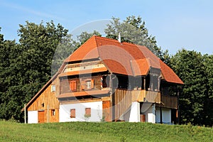 Renovated old wooden house with decorated details and stone foundation situated on top of the hill