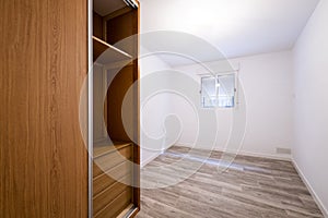 Renovated room with built-in wardrobe with sliding doors in cherry wood color, interior chest of drawers, white aluminum window