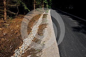 Renovation of asphalt road in the mountains. The ditches are filled with stones to slow down the water flowing out of the metal gr