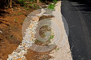 Renovation of asphalt road in the mountains. The ditches are filled with stones to slow down the water flowing out of the metal gr