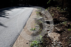 Renovation of asphalt road in the mountains. The ditches are filled with stones to slow down the water flowing out of the metal gr