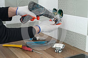 Renovation and construction in kitchen, close-up of electricians hand installing outlet on wall with ceramic tiles using
