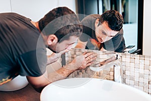 renovation details. Construction details with handyman or worker adding mosaic ceramic tiles on bathroom walls