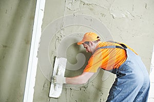 Renovation at home. Plasterer smoothing plaster on wall.