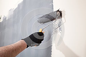 Renovation of interior. Man hand holds paint roller and painting wall with grey color.