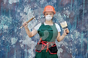 Renovation and remodelling concept. Woman in helmet and protective mask posing with hammer and spatula