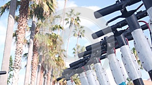 Rental electric scooters parked on street sidewalk, palm trees, California, USA.