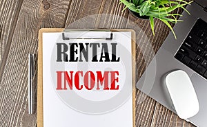 RENTAL INCOME text on paper clipboard with laptop and mouse on wooden background , business concept