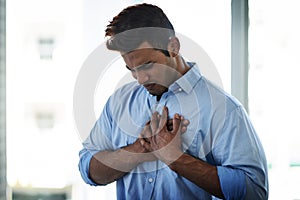 Reoccurring pain should be treated immediately. Shot of a young businessman suffering with chest pain at work.
