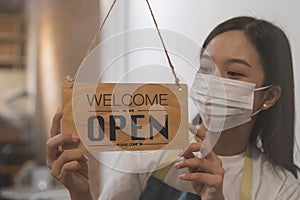 Reopen, asian young owner retail, coffee shop woman turning sign board open wearing face mask, protect to pandemic of coronavirus