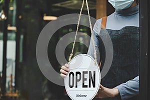 Reopen. friendly waitress wearing protection face mask turning open sign board on glass door in modern cafe coffee shop, cafe rest